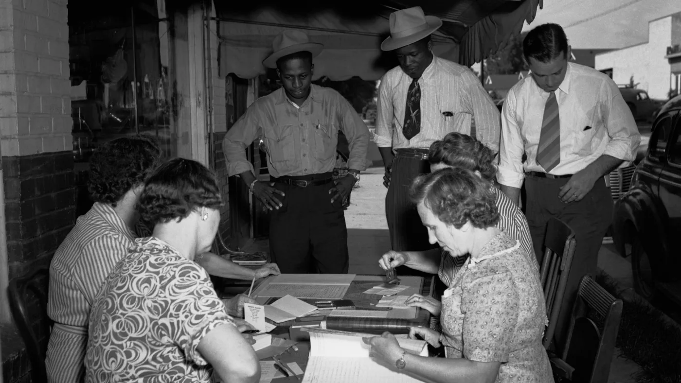 Two black men standing at a table of white vote administrators